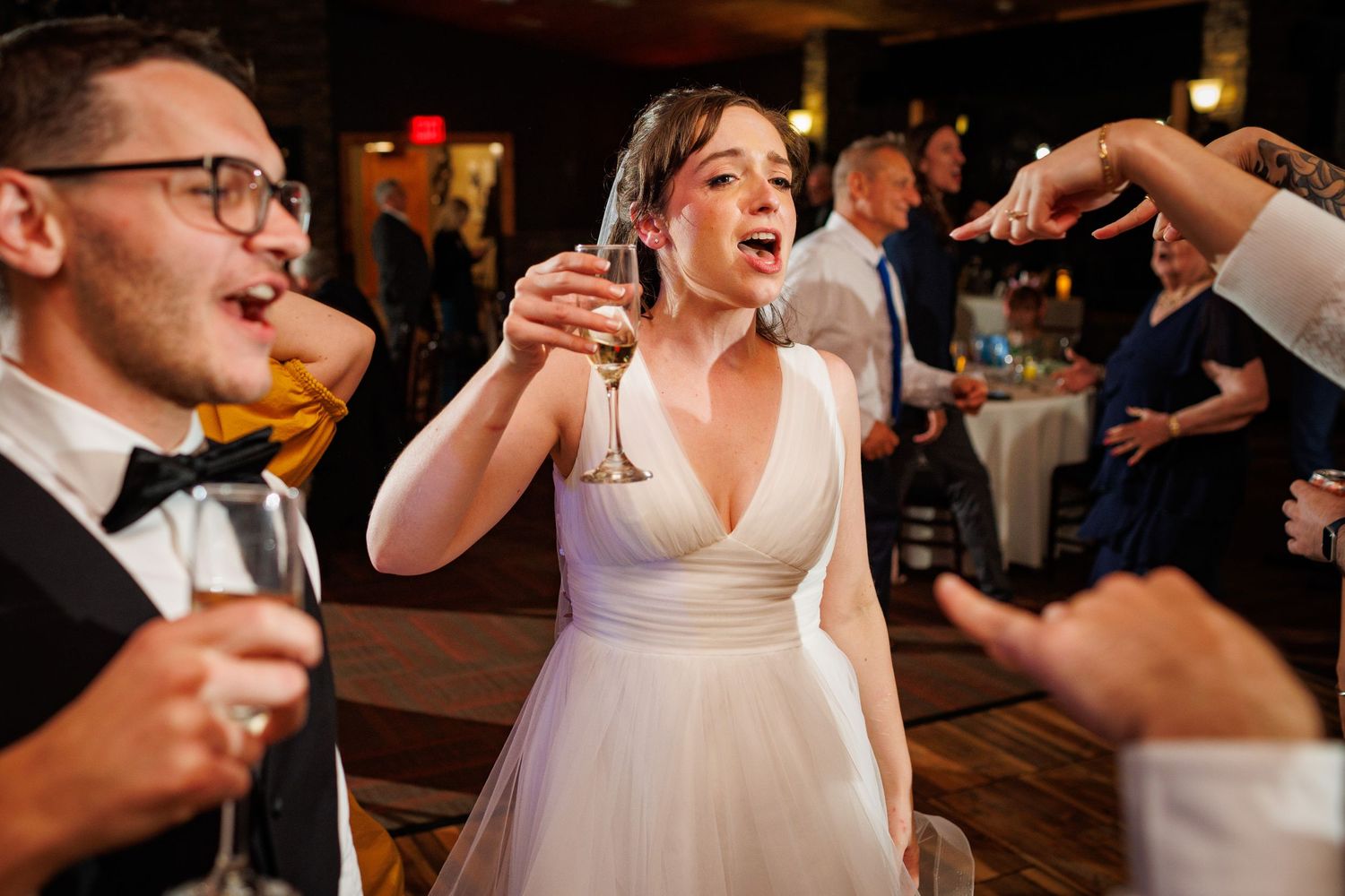 Bride in white gown raises champagne glass joyfully while celebrating at wedding reception.