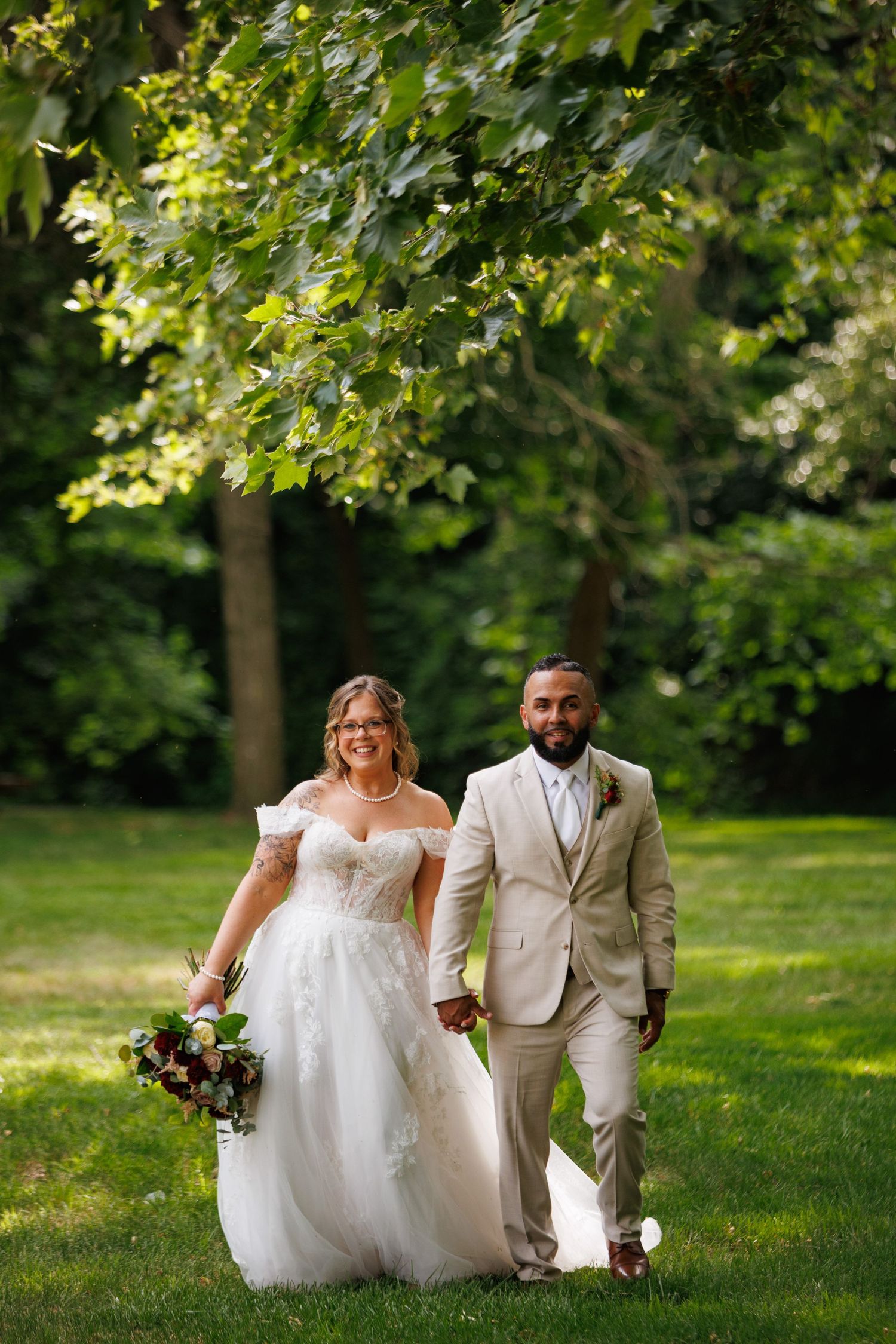 Smiling bride and groom walking hand in hand through a lush green park on their wedding day.