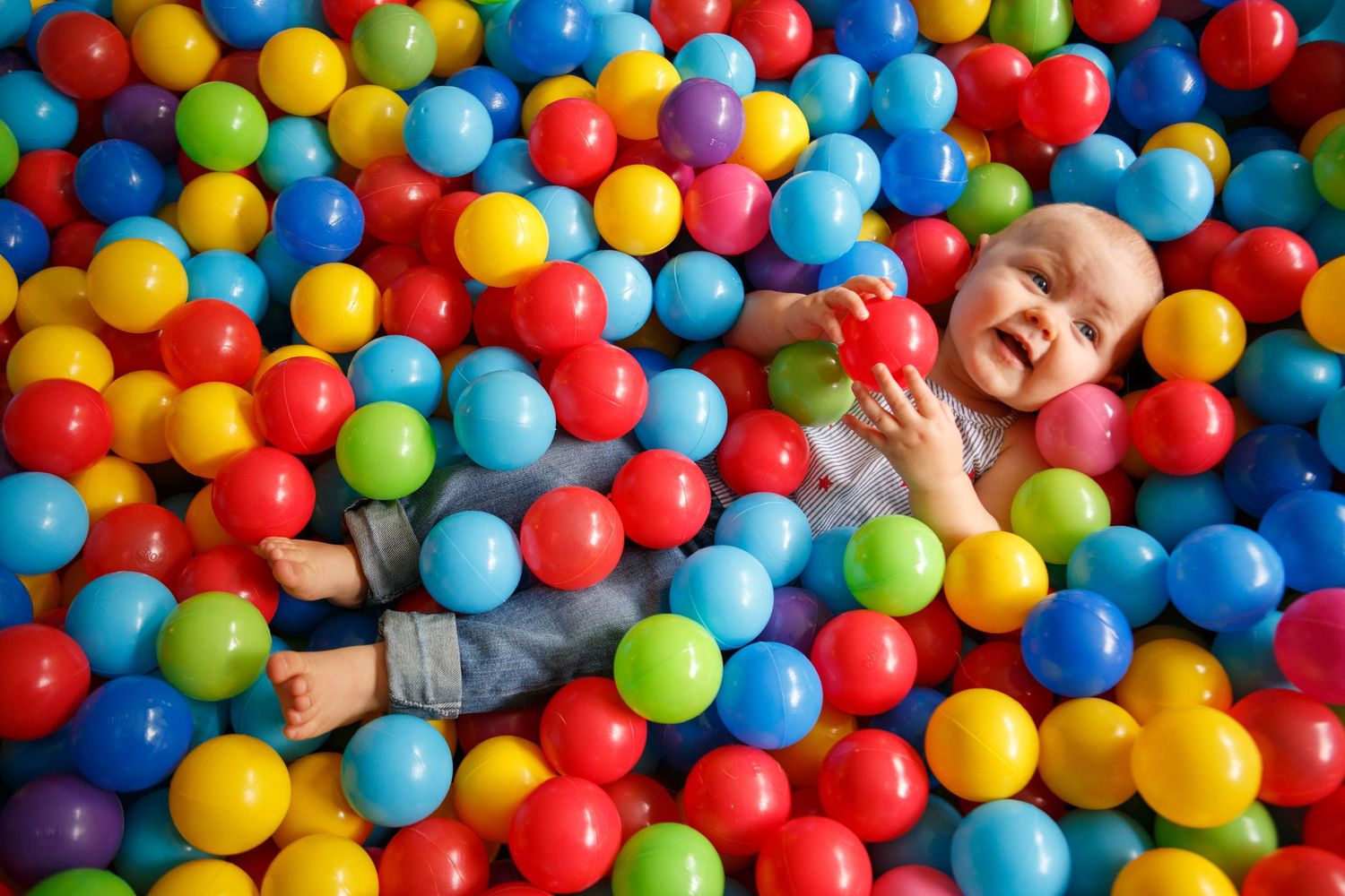 Colorful ball pit filled with red, yellow, blue and green plastic balls creating a vibrant playful scene.