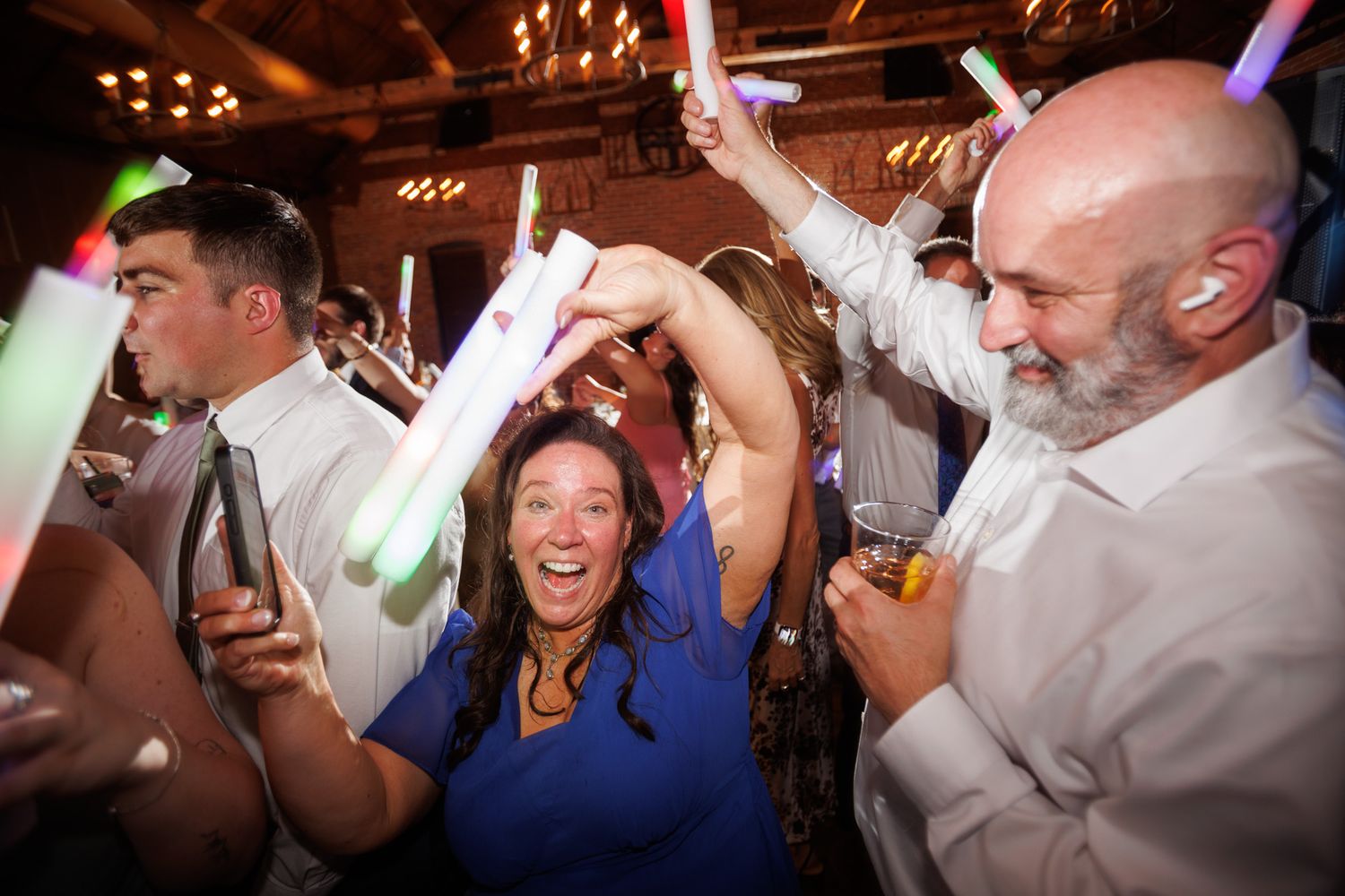 Excited wedding guests dancing with colorful glow sticks at a lively reception party.