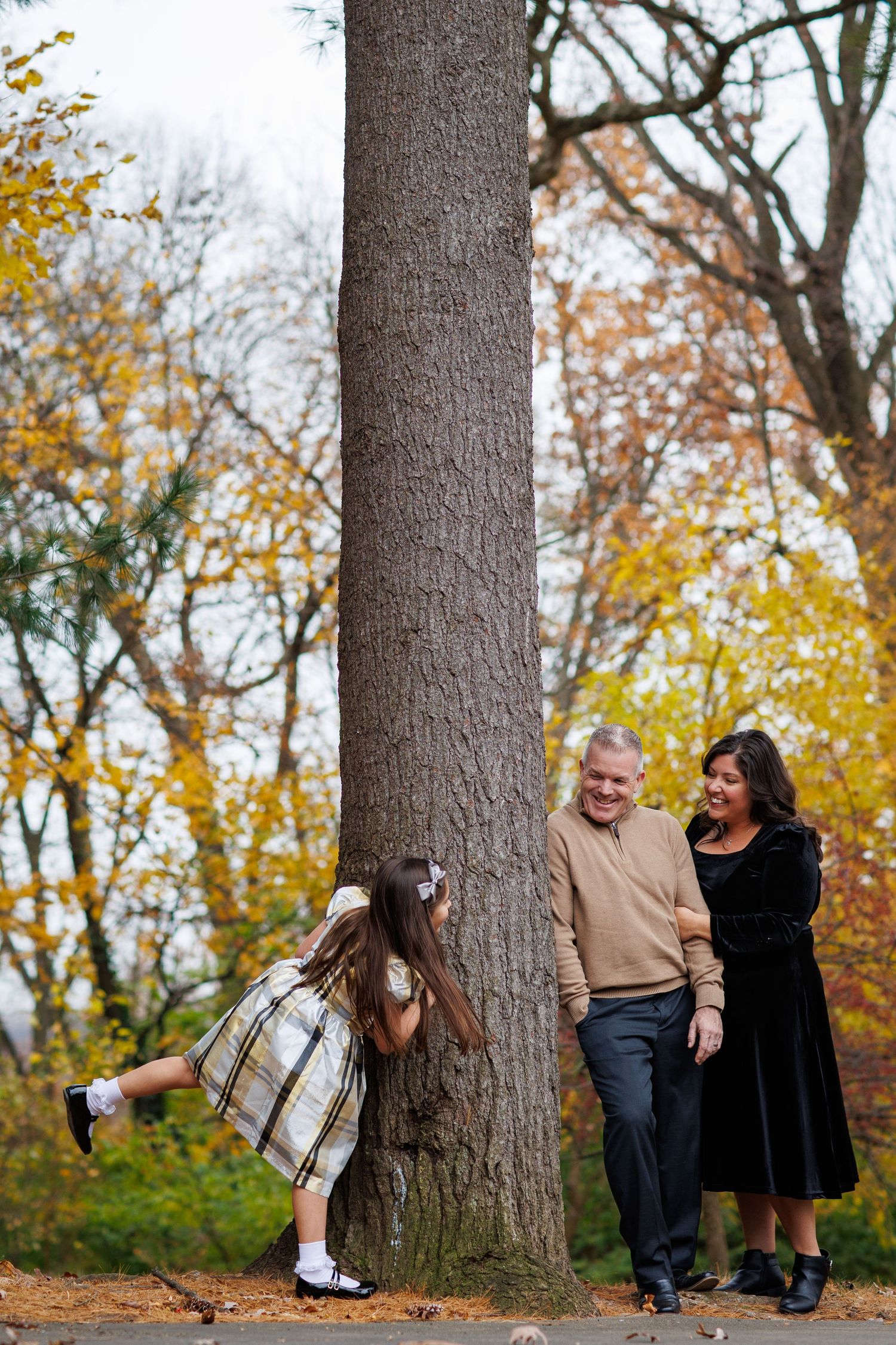 A series of playful poses against a large tree trunk in a park with vibrant autumn foliage in the background.