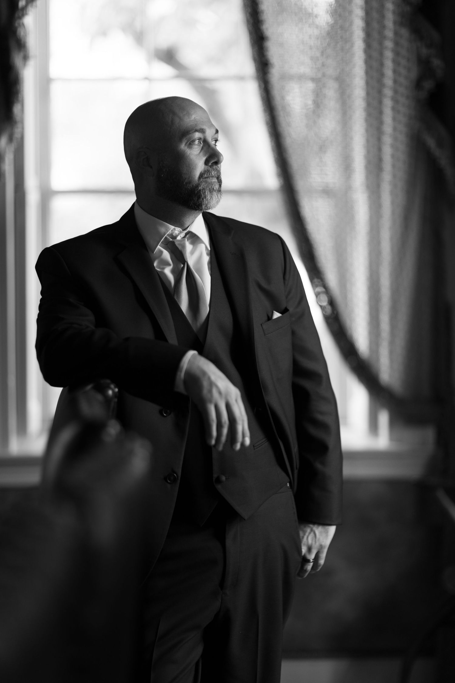 Black and white portrait of men in formal attire standing near windows.
