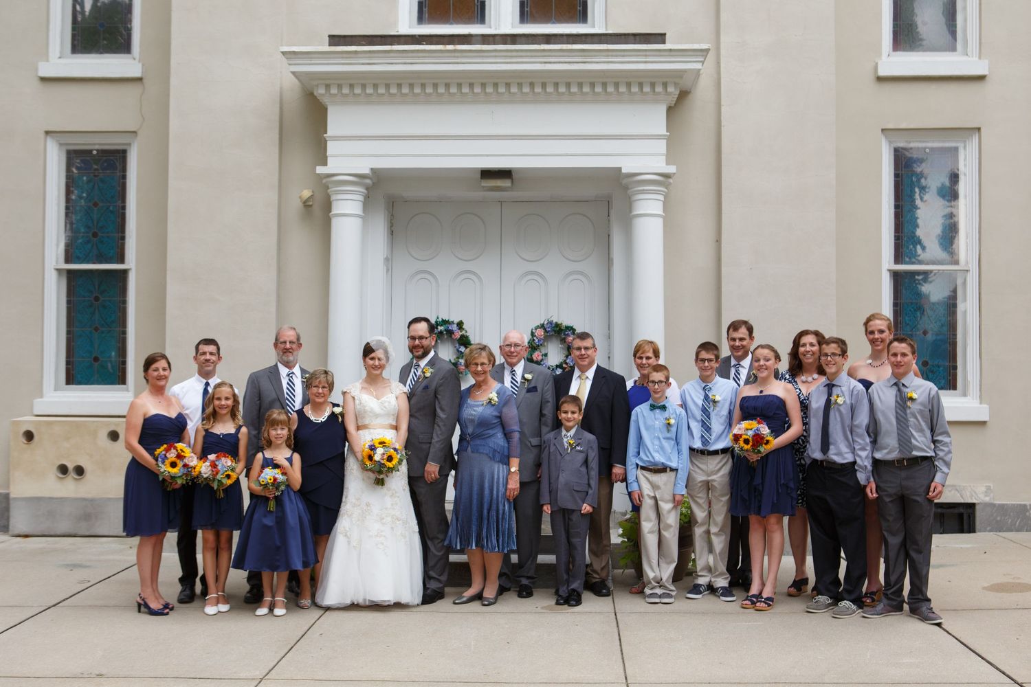 Wedding party poses together in front of a classic white building with ornate columns and doorway.