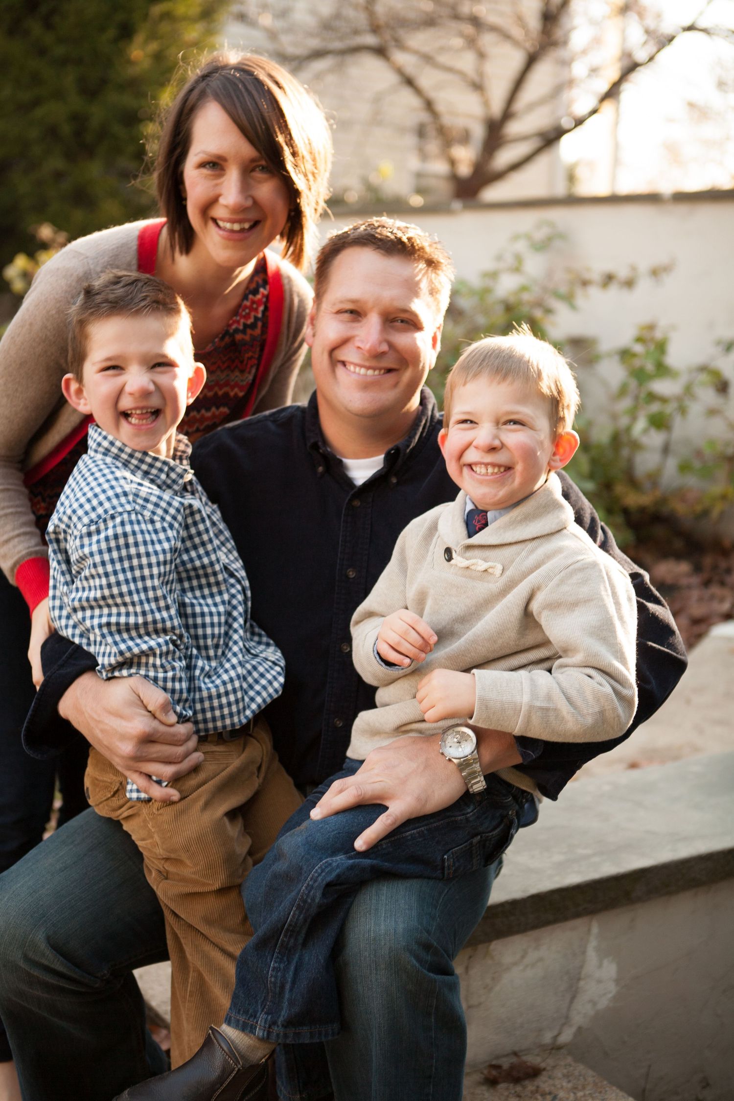 Family portrait session outdoors with parents and children laughing together on a bench.