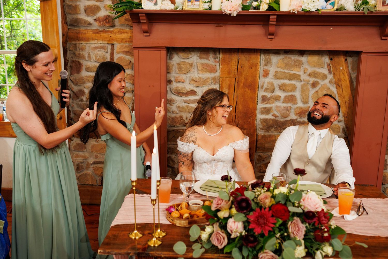 Bridesmaids in sage green give toast to laughing bride and groom at wedding reception.