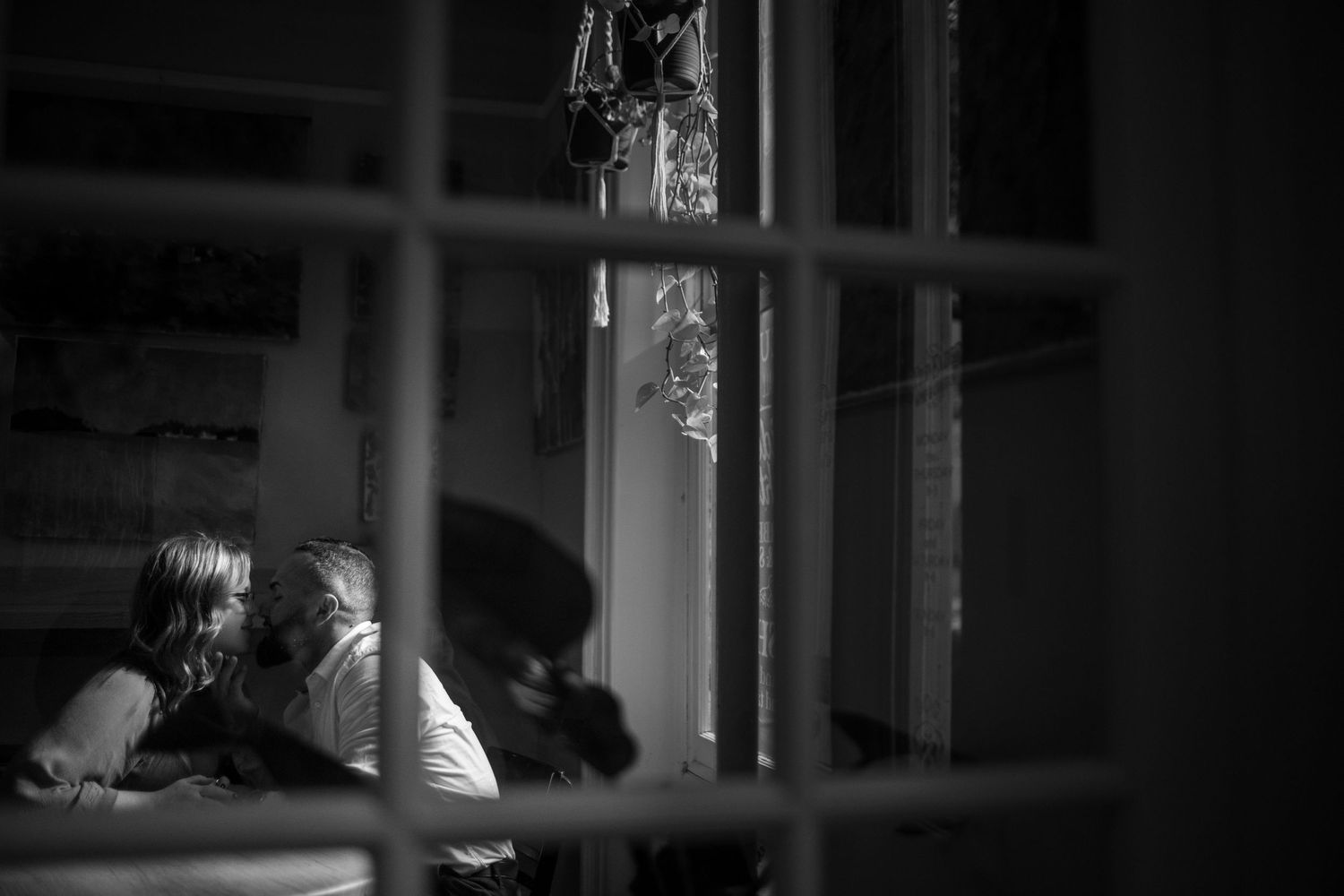 A dramatic black and white film noir style scene showing a person looking through window blinds in darkness.