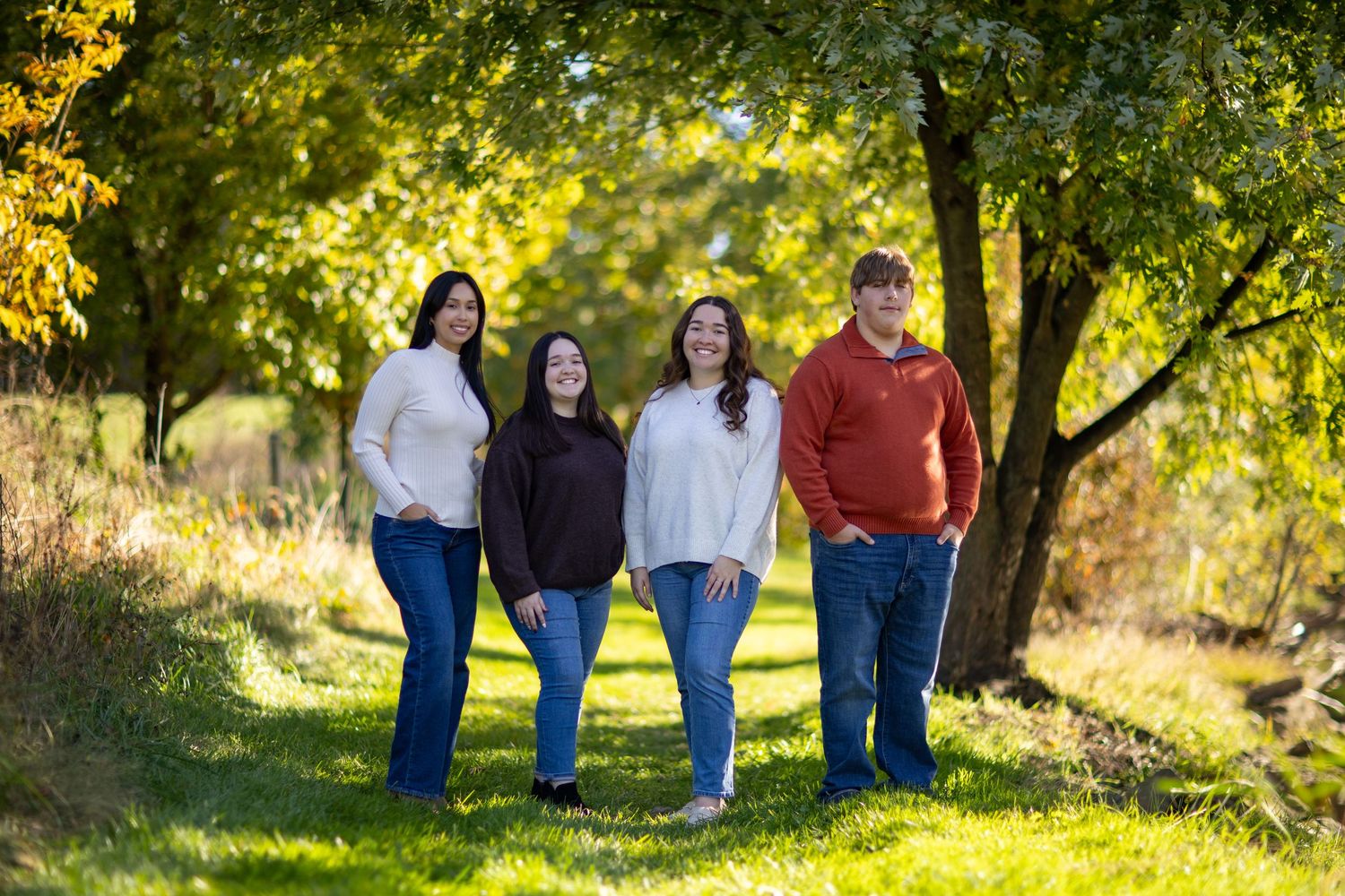A group of people pose together in a sunlit autumn forest setting with golden leaves in the background.