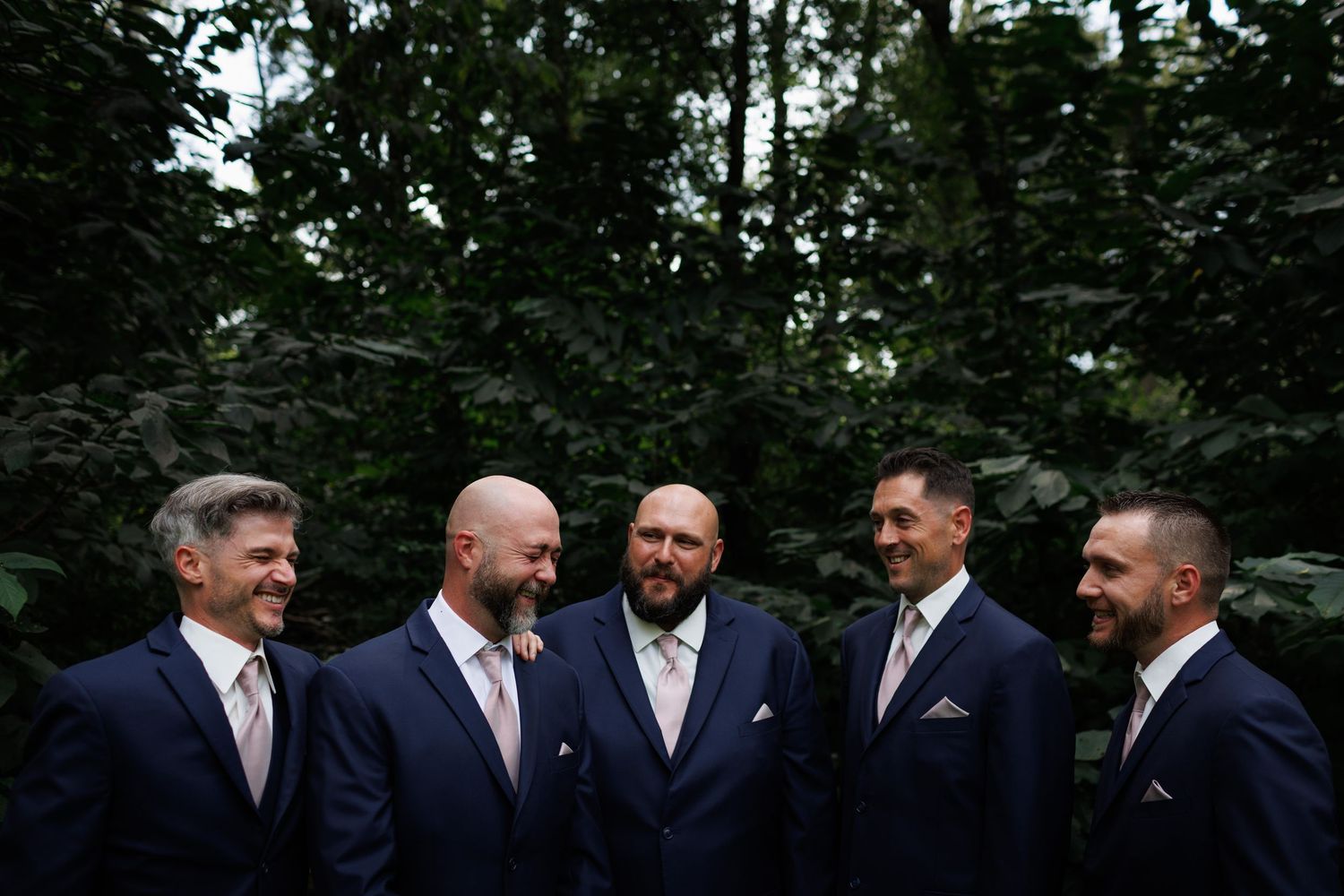 A group of men in dark suits and ties standing together outdoors in a garden setting.