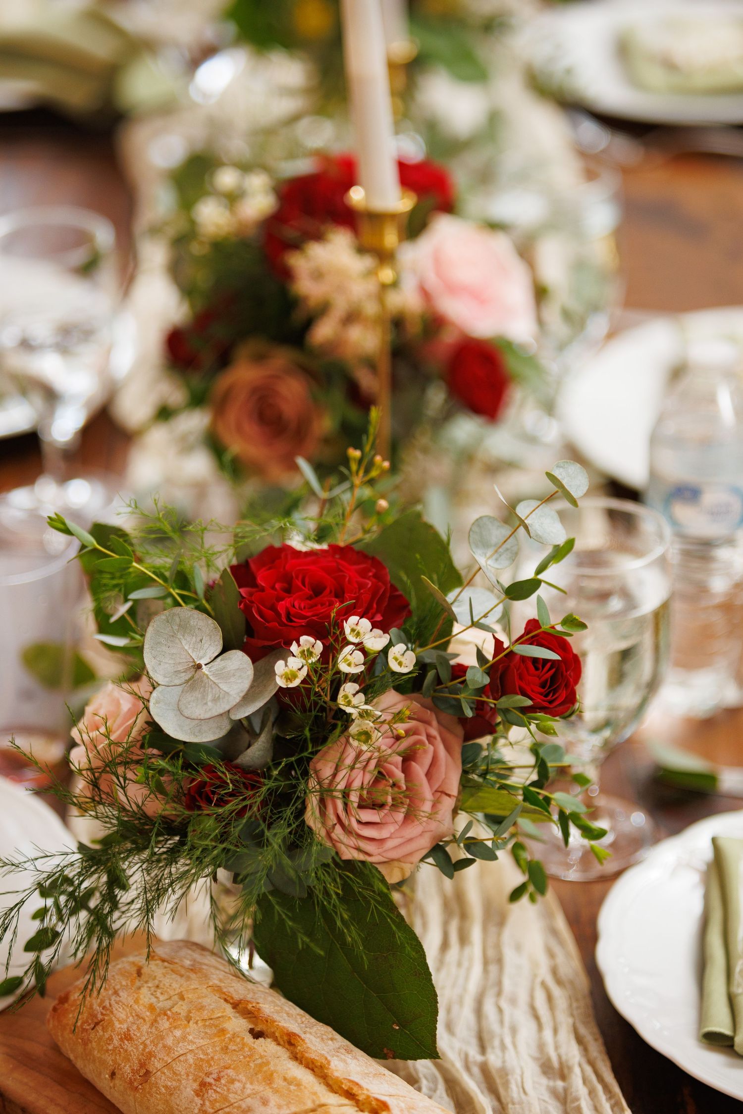 Elegant wedding table with red and pink rose centerpiece, greenery, candles, and rustic bread on a decorated dining table.