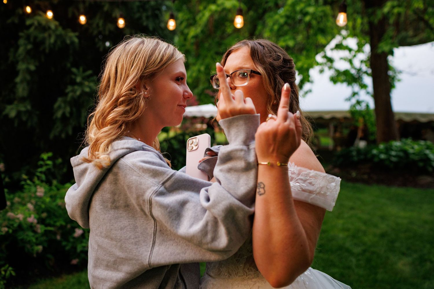 Two women dance together outdoors at evening wedding reception under string lights.