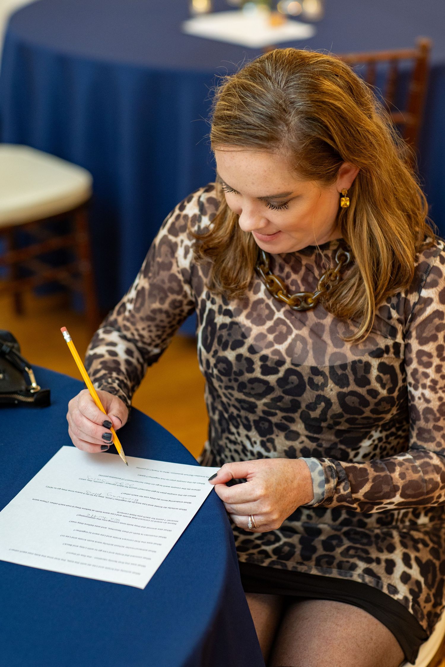 Person wearing leopard print top writing on paper with yellow pencil in indoor setting.