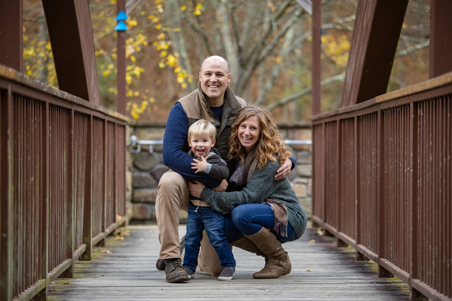 Family enjoying autumn weather while walking on a wooden bridge in a forest park.