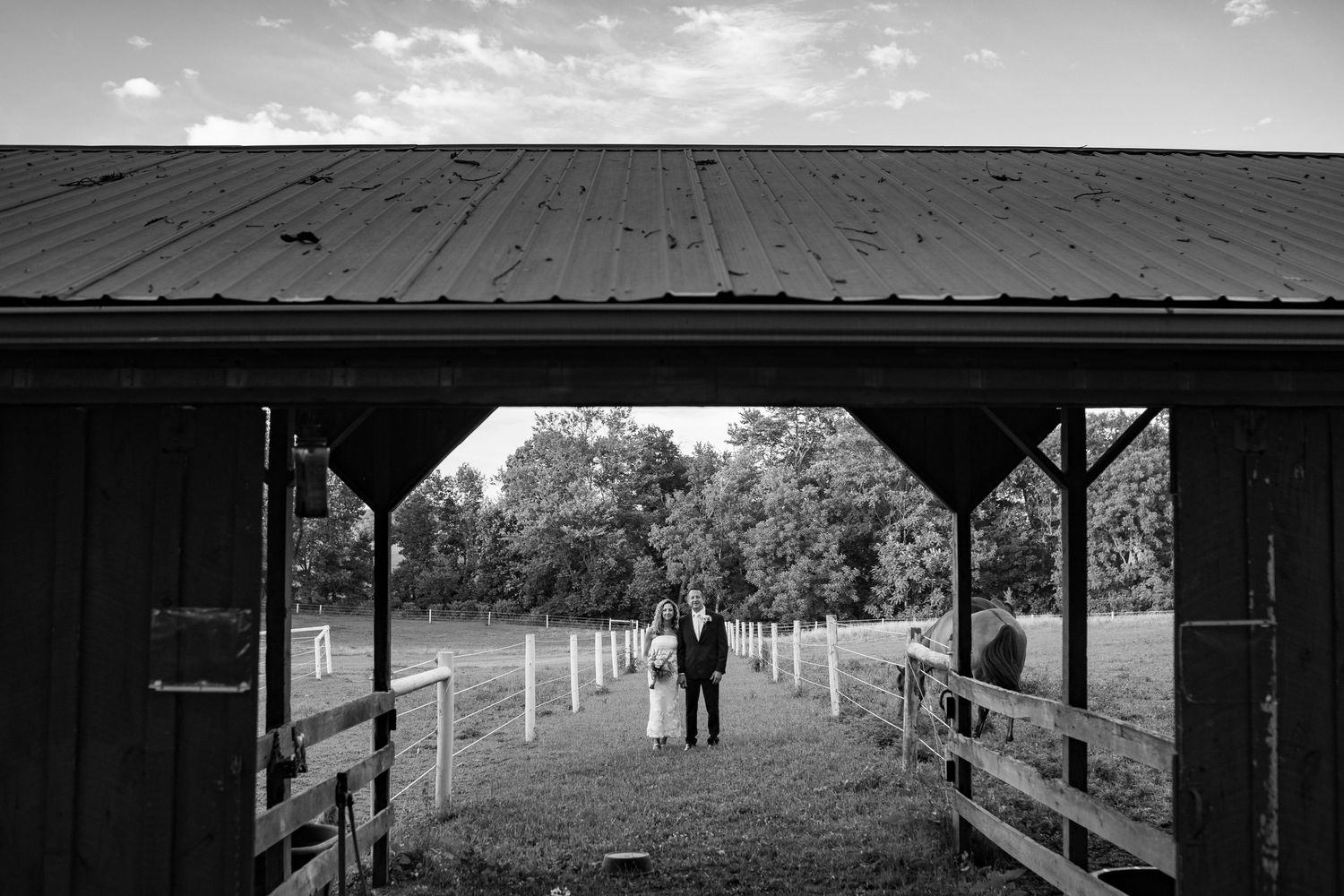 Black and white photo of a bride and groom standing in a barn doorway on a farm.