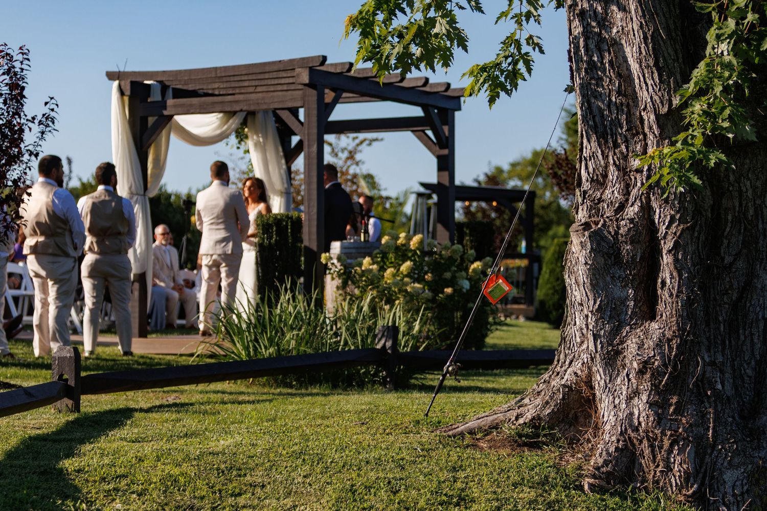 A wooden pergola stands in a beautiful garden setting during an outdoor gathering on a sunny day.