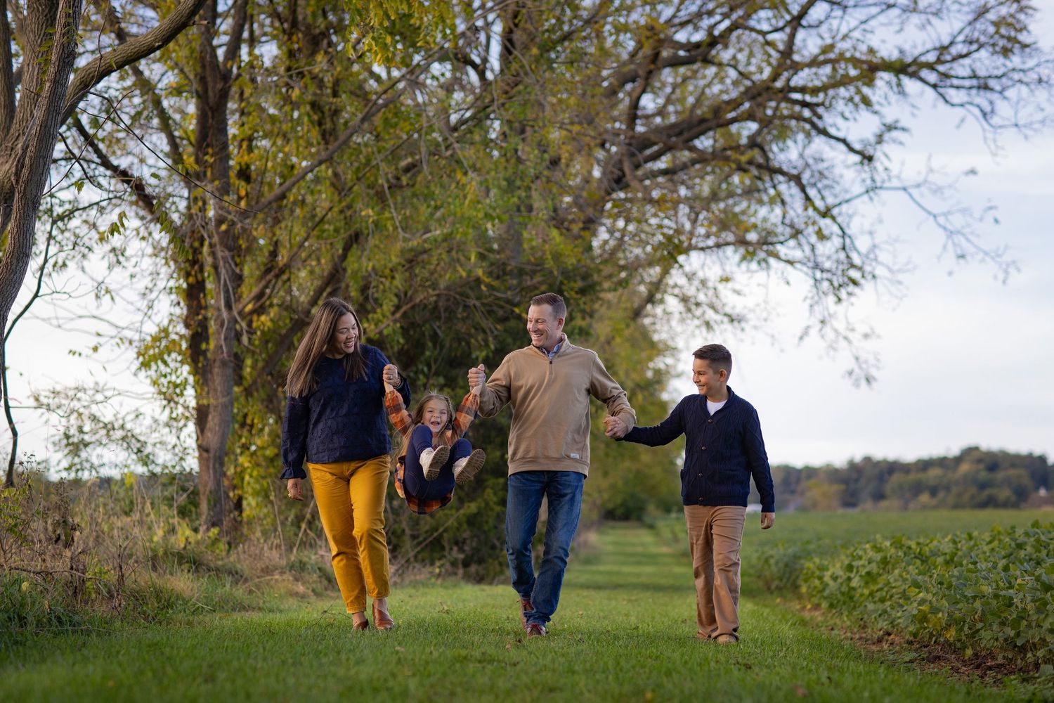 A family of three enjoys an autumn walk together on a tree-lined dirt path in nature.