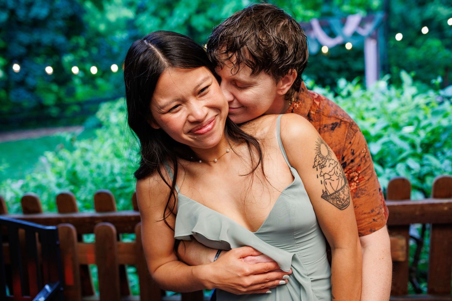 Couple sharing a tender embrace outdoors at evening wedding reception with string lights.