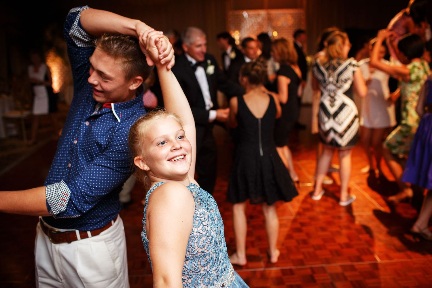 Young dancers twirl and spin together on a dance floor during a formal event with a red carpet.