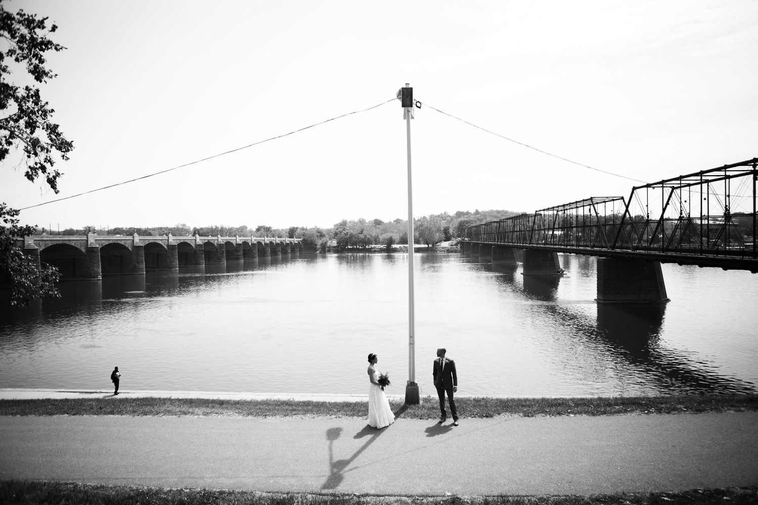 Black and white landscape of people silhouetted near bridge over calm water.