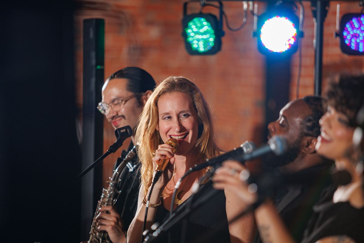 Live wedding band performing with female vocalist singing into microphone on stage.