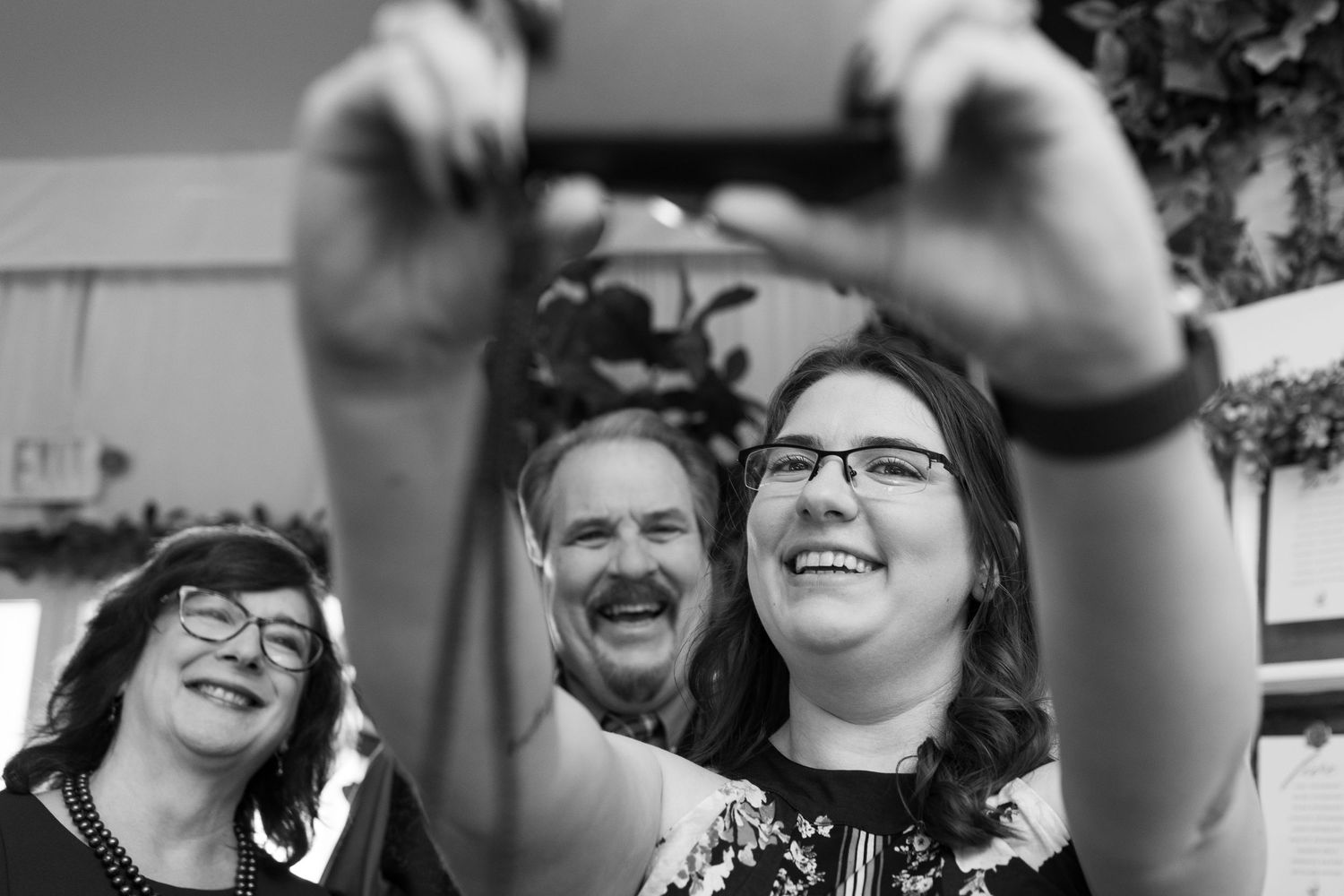Joyful people laugh while someone in the foreground takes a selfie in black and white photography.