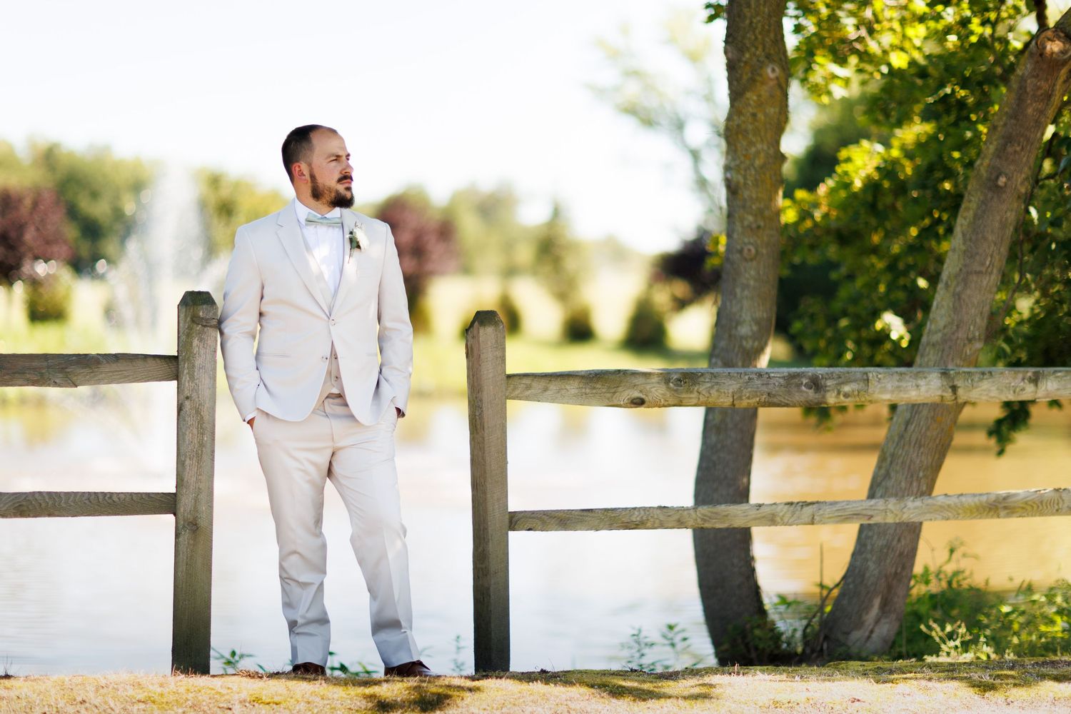 A wedding party poses outdoors near a rustic wooden fence at sunset for candid photographs.
