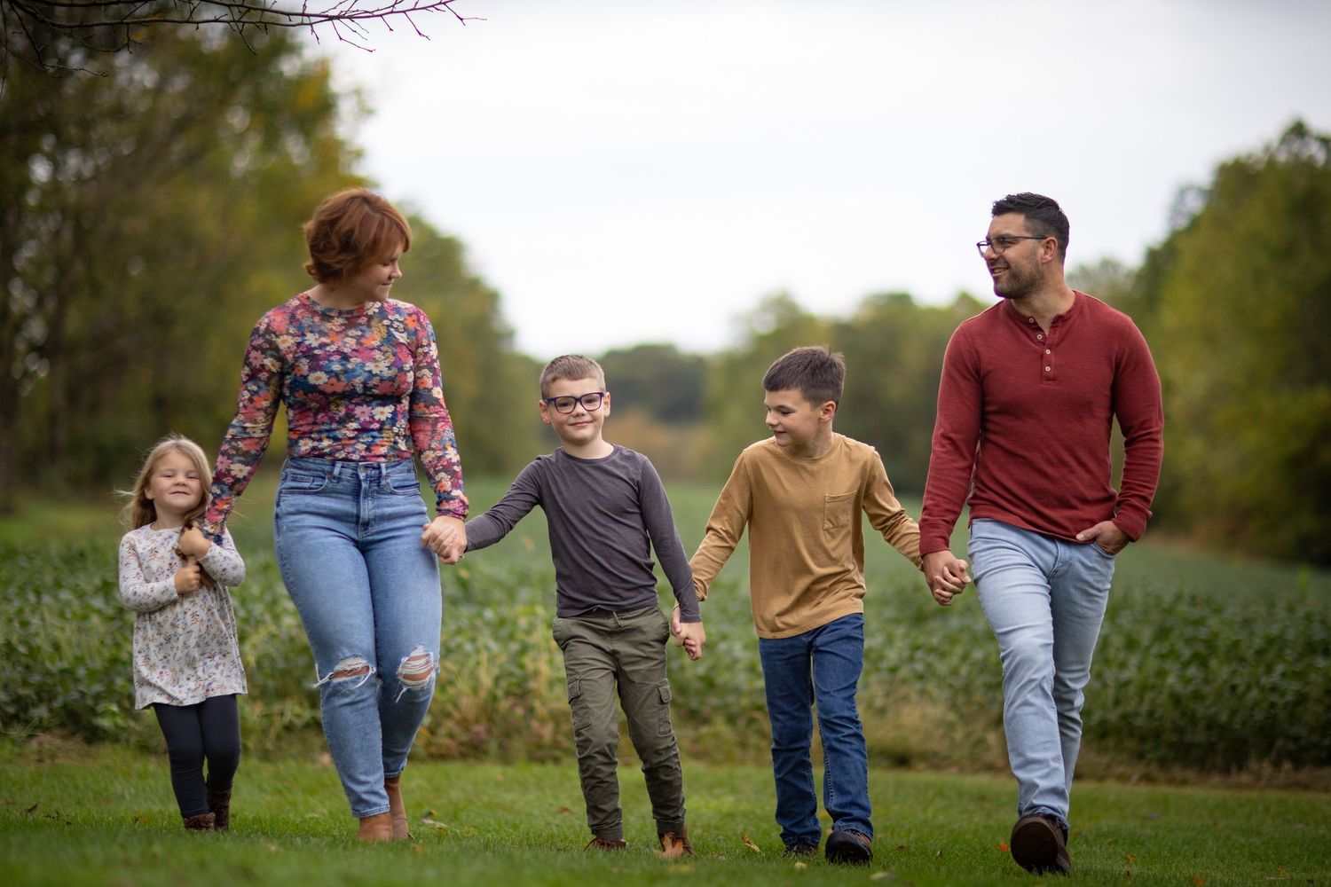 A family enjoys a casual walk together on a grassy path surrounded by lush greenery on an overcast day.