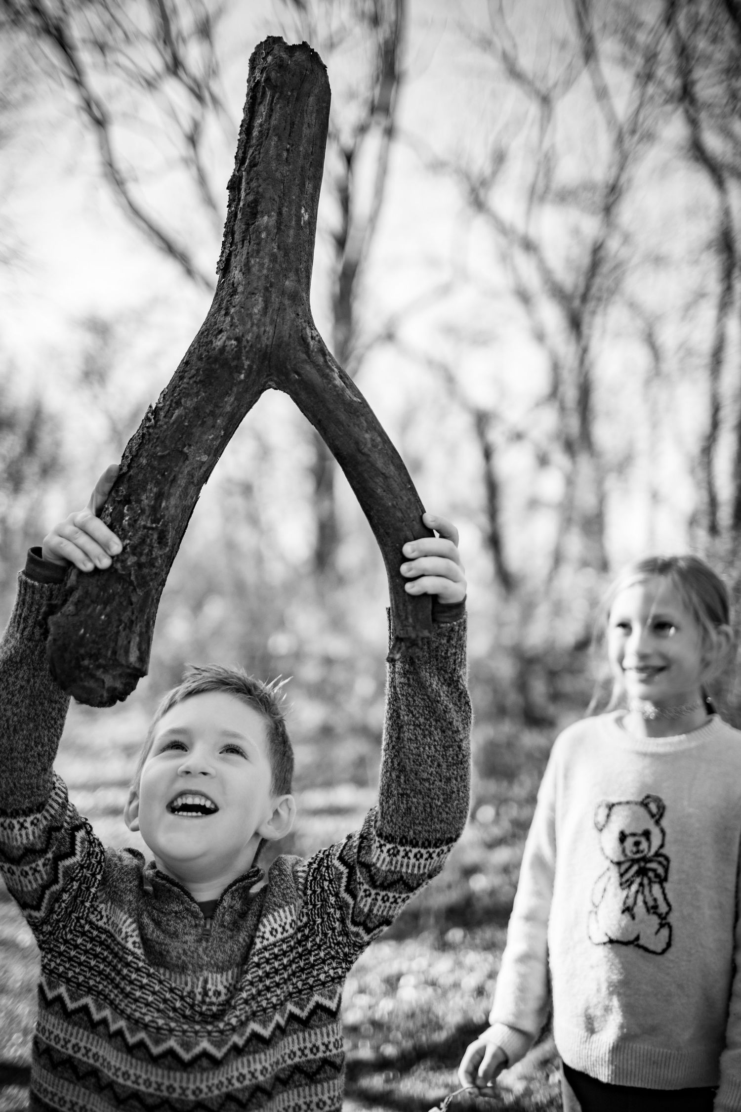 Black and white photo of joyful moments between trees in a wooded setting.