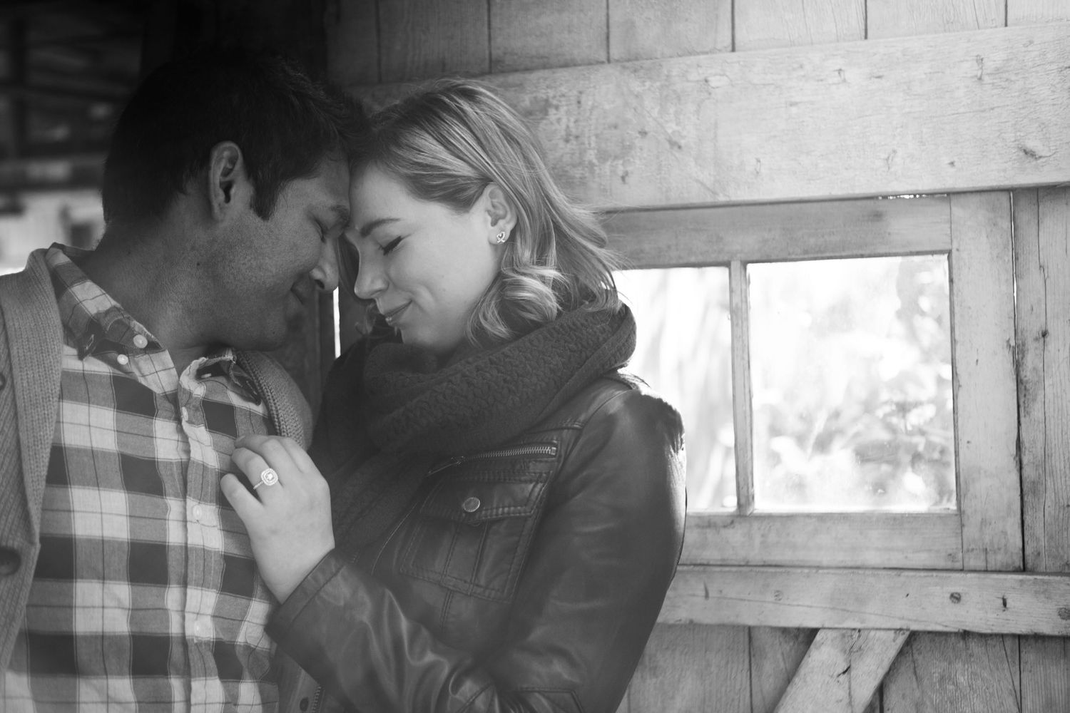 Intimate black and white portrait of couple sharing tender moment by window.