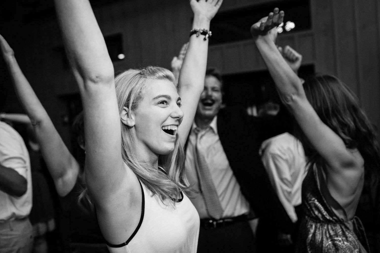 A group of people dancing joyfully at a party with their arms raised up in black and white photography.