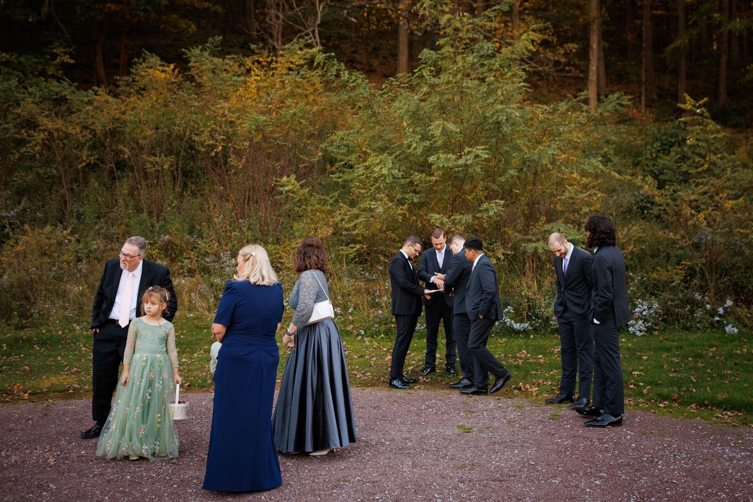 Wedding guests mingle outdoors near autumn forest in colorful fall wedding celebration photo.