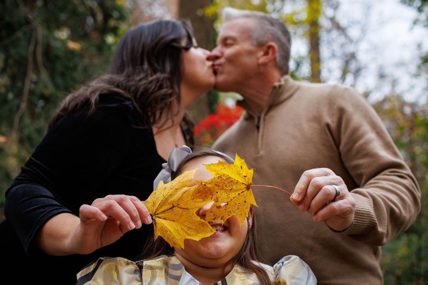 A couple shares an autumn moment outdoors while holding colorful fallen maple leaves.