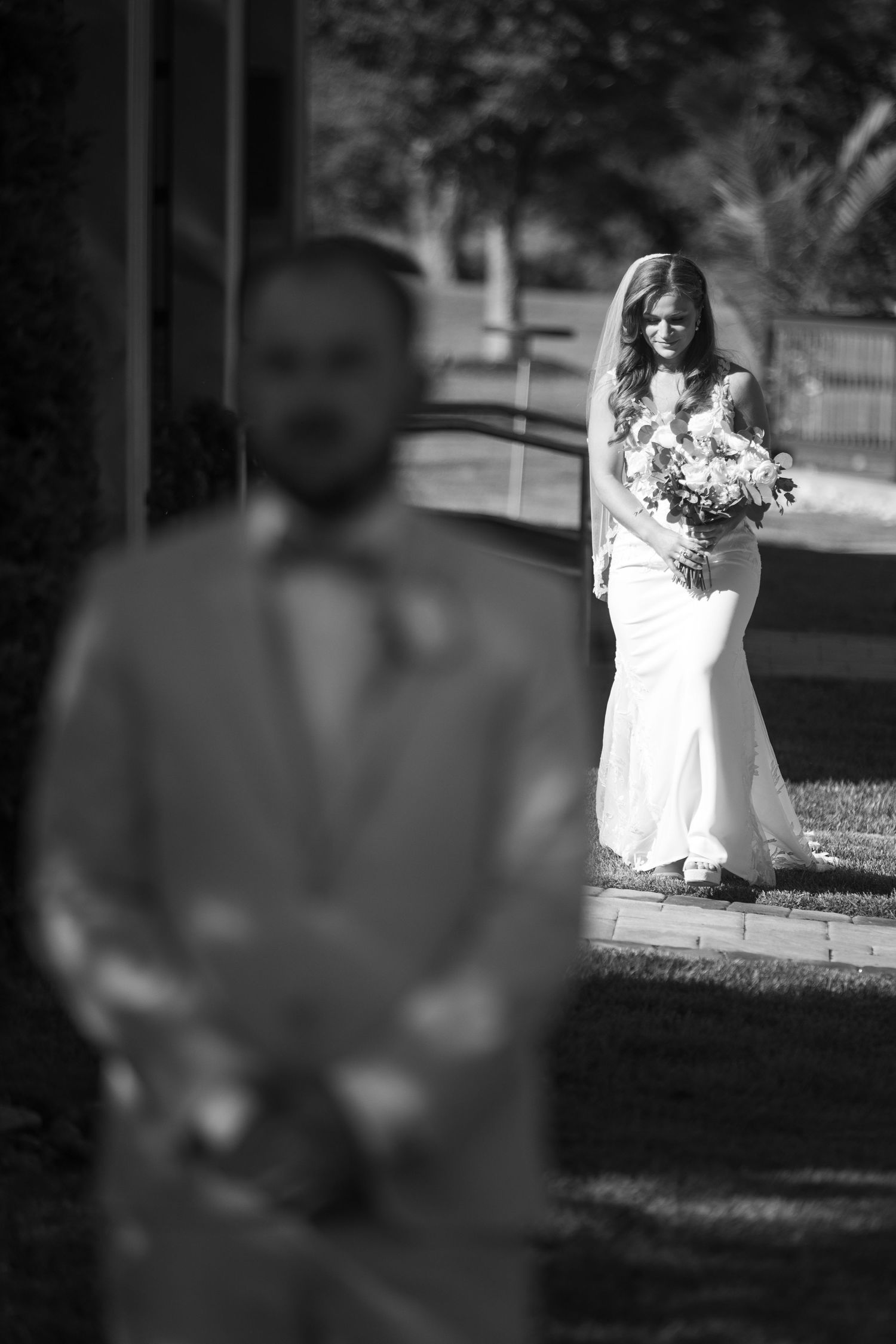 A bride in a white wedding dress poses with her bouquet in a sun-drenched garden setting.