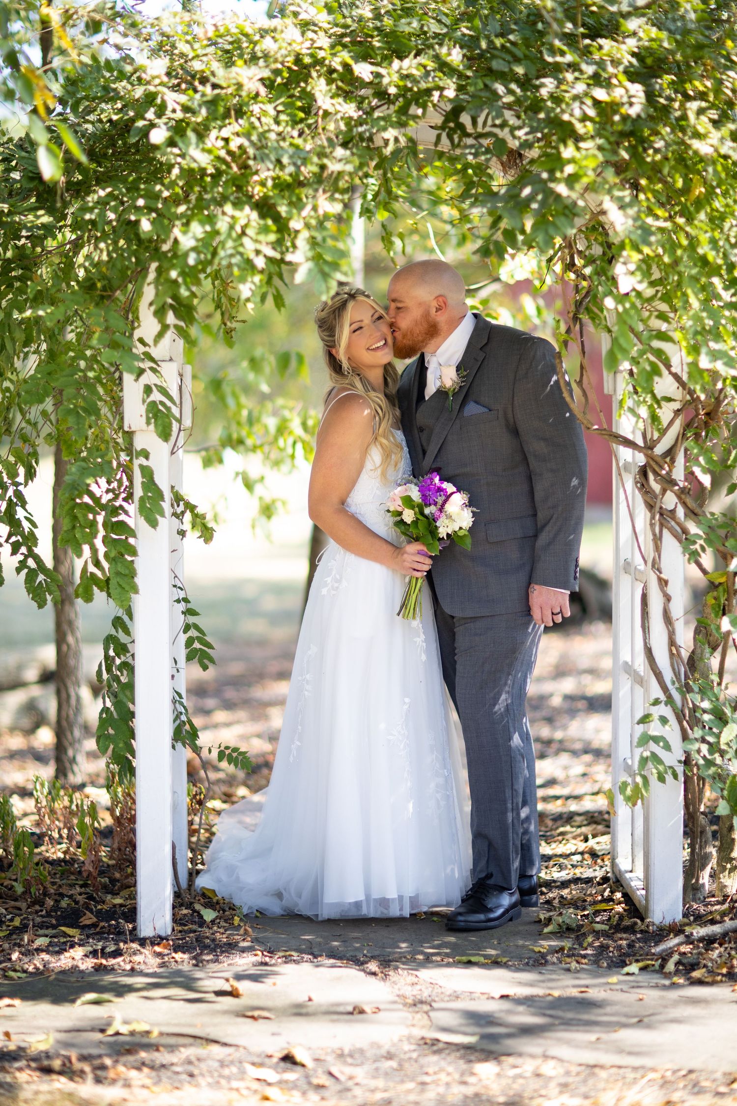A couple shares romantic moments in a sun-dappled grove with white trees and natural lighting creating a beautiful setting.