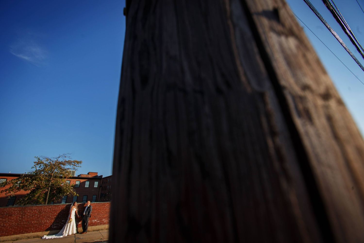 Artistic wide-angle shot of wedding couple by wooden fence post.