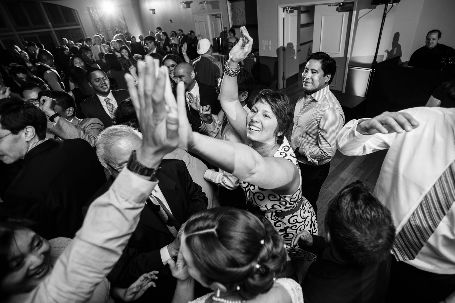 Black and white photo of energetic dancing at a wedding reception with guests on a crowded dance floor.