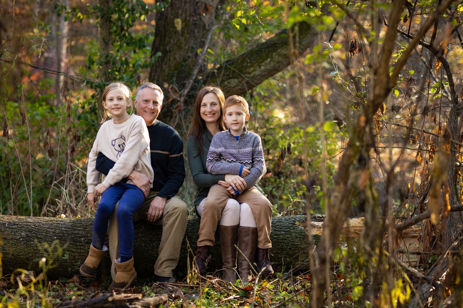 Family sits together on a rustic wooden bench surrounded by autumn foliage.