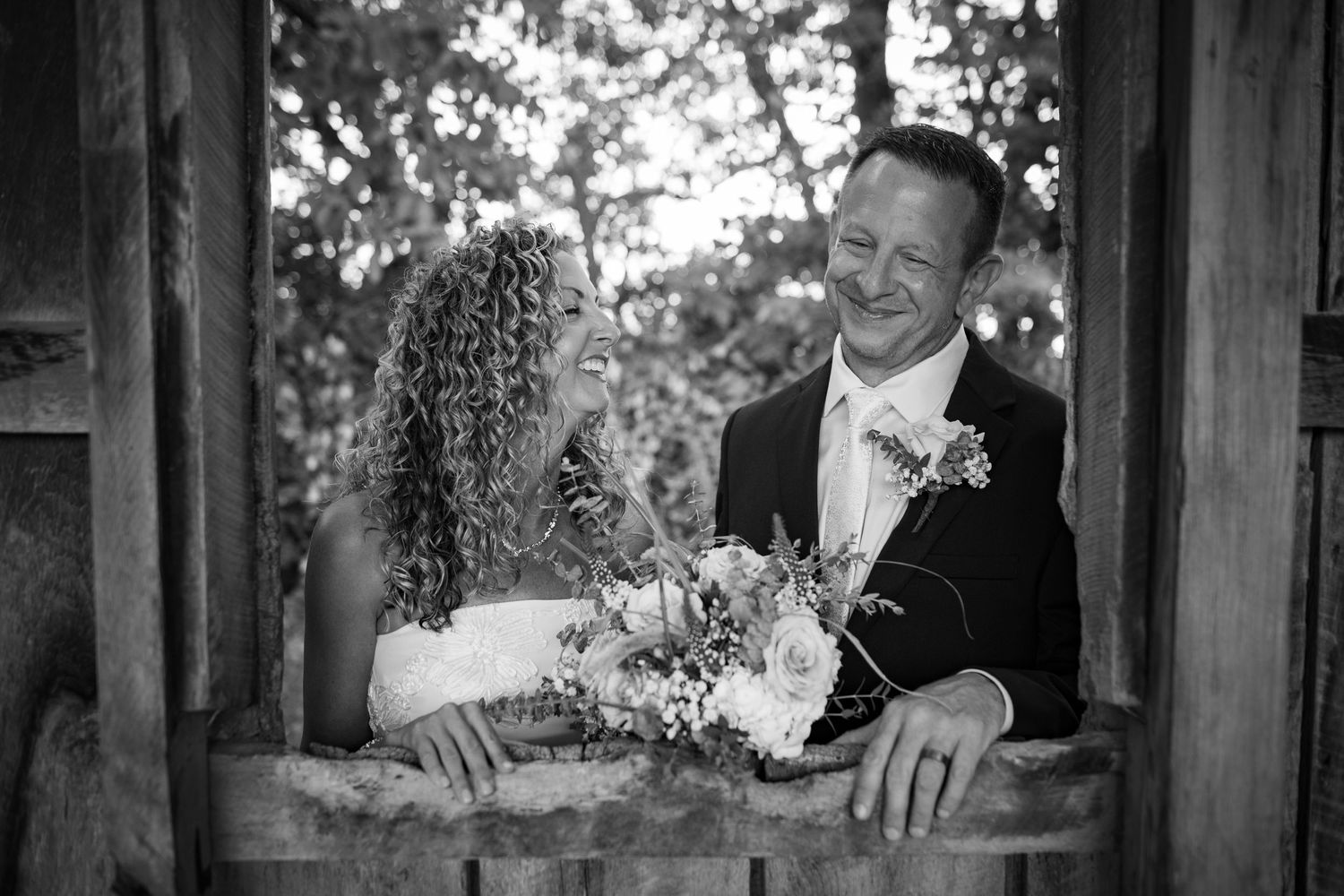 Bride and groom laughing together in black and white wedding portrait at rustic barn.