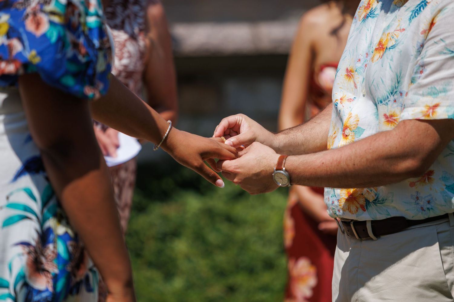 Man in floral shirt placing a bracelet on a woman's wrist outdoors at a summer event.