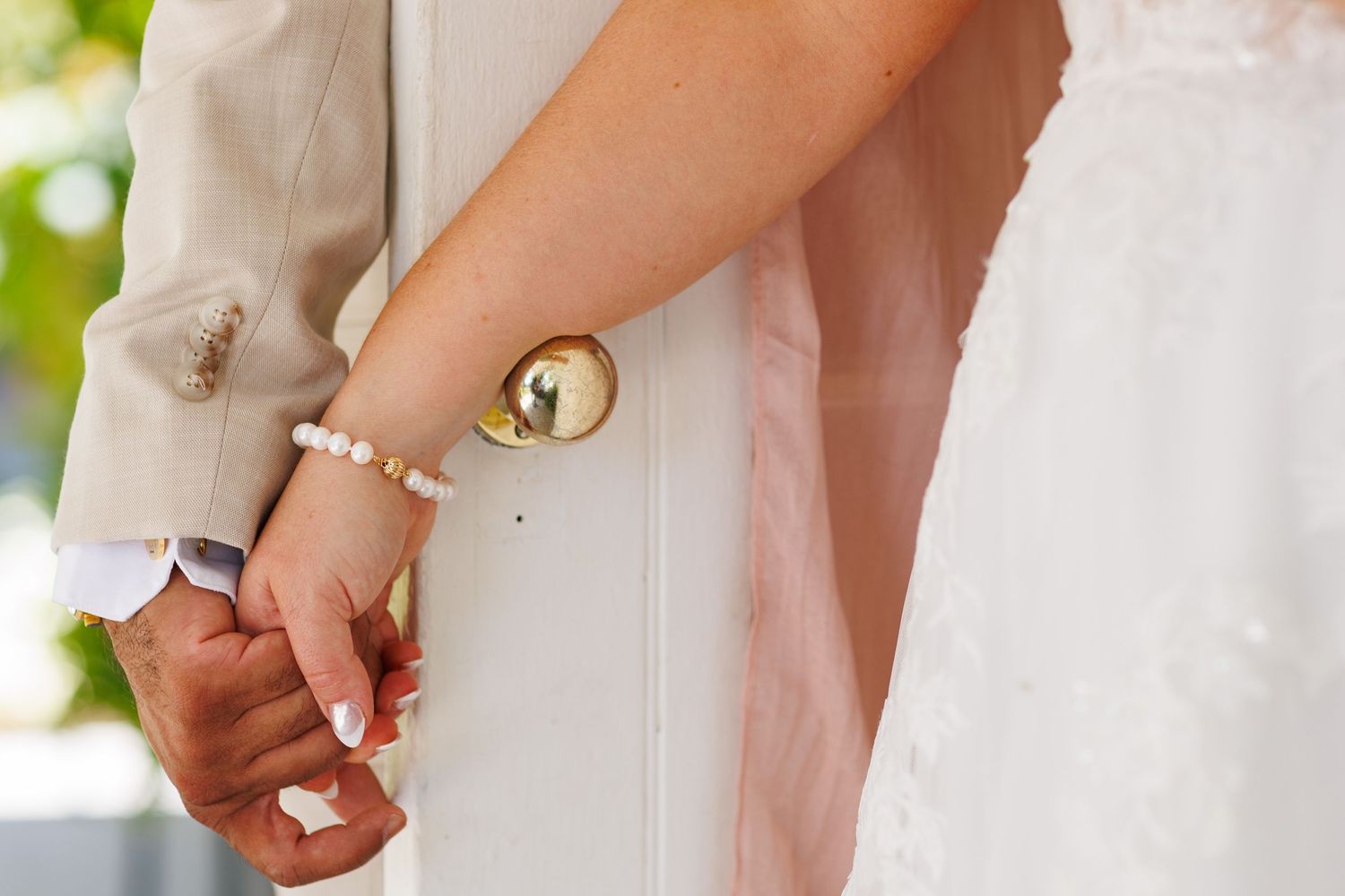 Bride and groom holding hands at wedding ceremony, bride wearing pearl bracelet and gold watch.