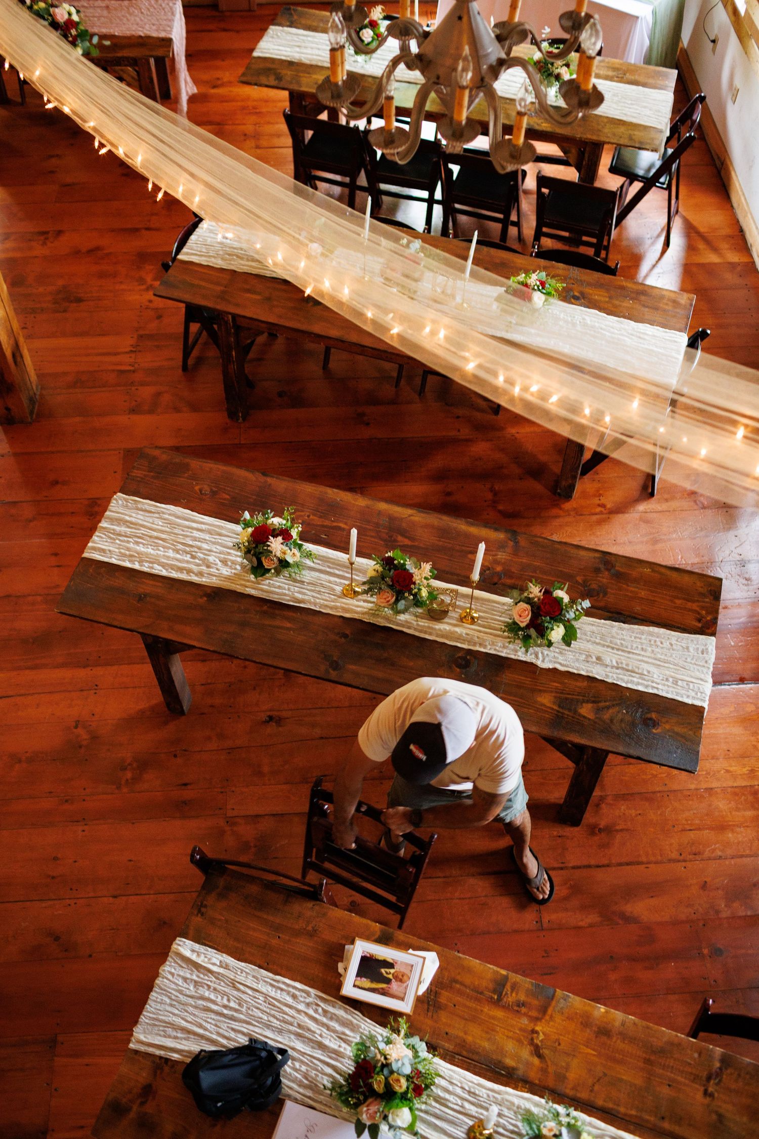 Aerial view of rustic wooden farm tables decorated with floral centerpieces and white runners for an elegant wedding reception.