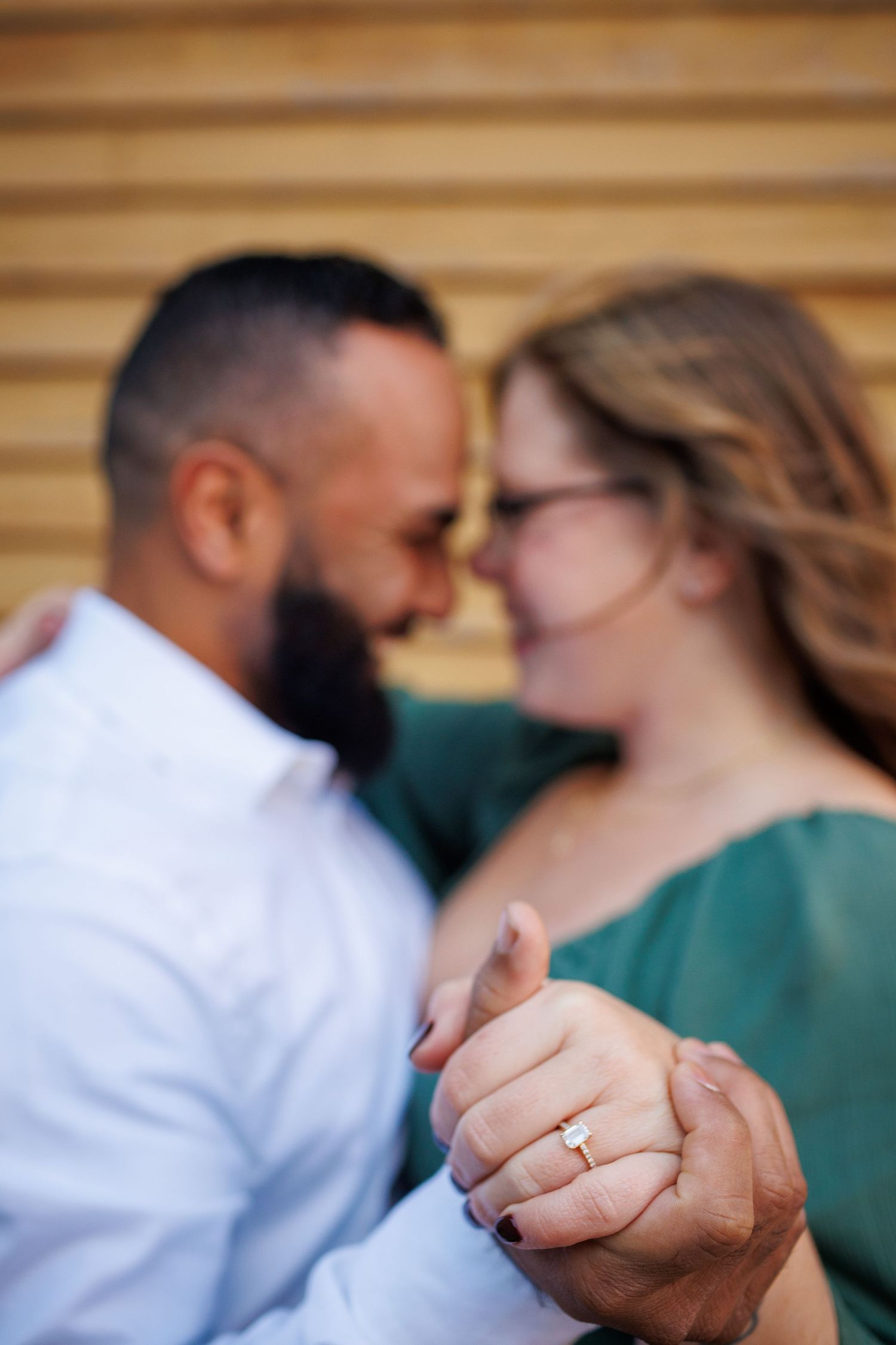 Close-up of hands wearing wedding rings as a couple shares an intimate moment in the background.