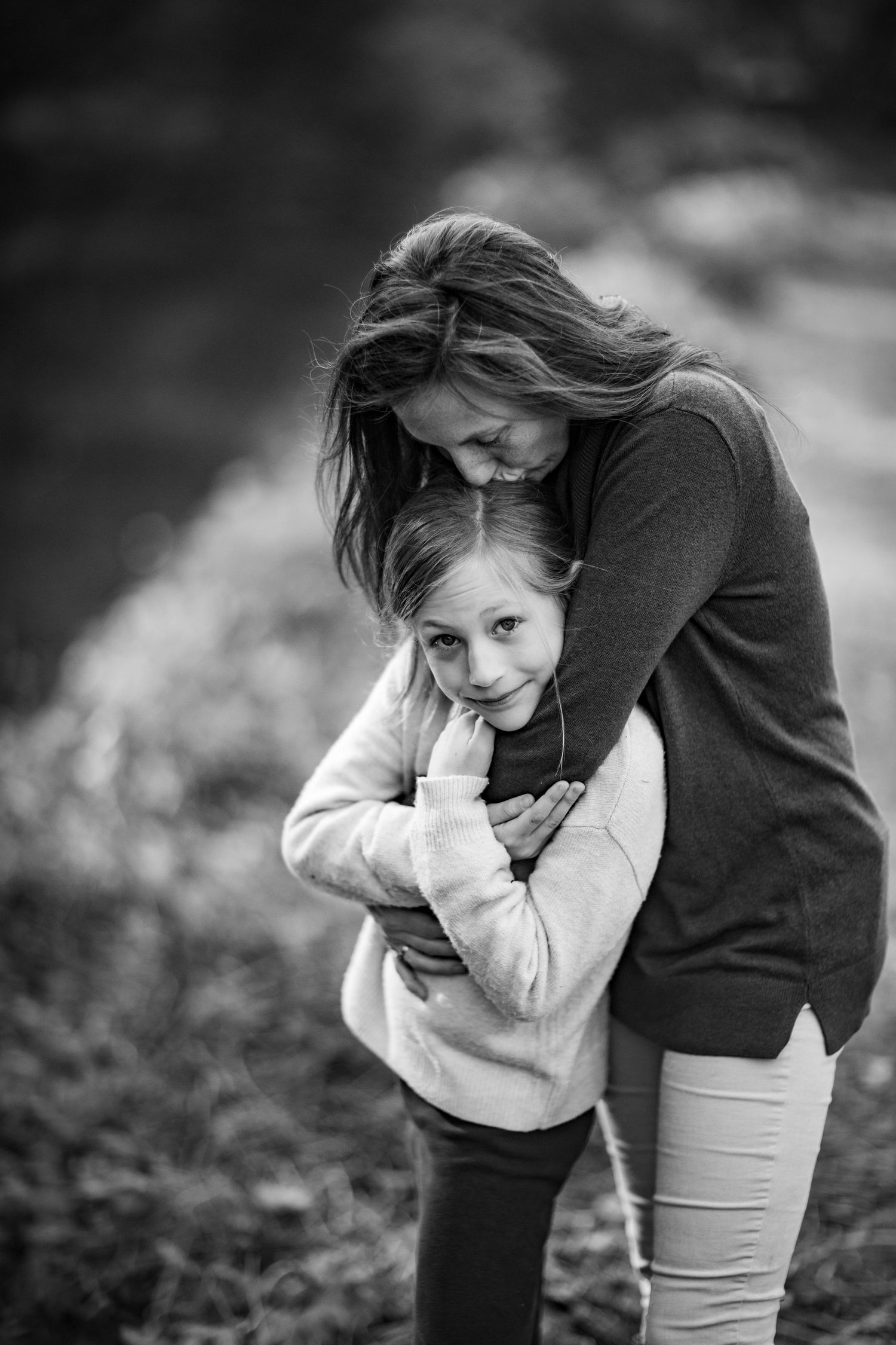 Intimate black and white portrait showing tender embrace against natural outdoor backdrop.