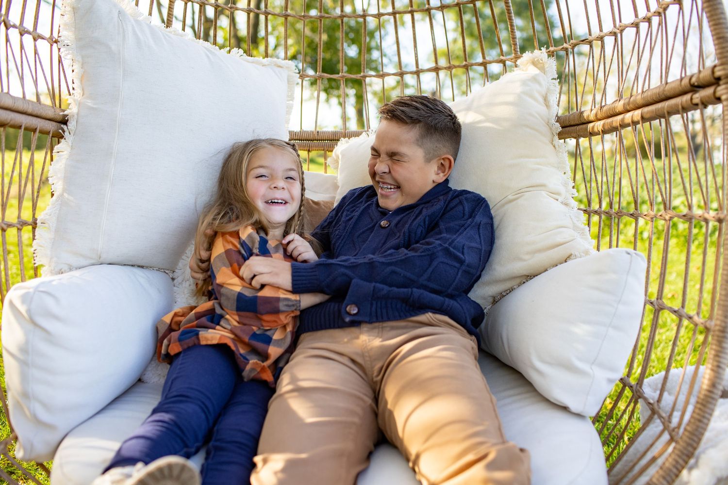 A couple relaxes on a cozy hanging rattan chair in an outdoor garden setting.
