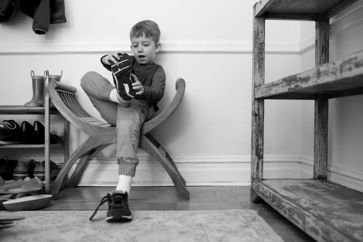 A young baseball player sits on a wooden bench in a locker room holding their glove in black and white.