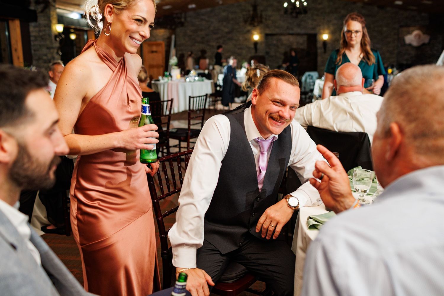 Wedding guests laugh and interact joyfully during lively indoor wedding reception celebration.