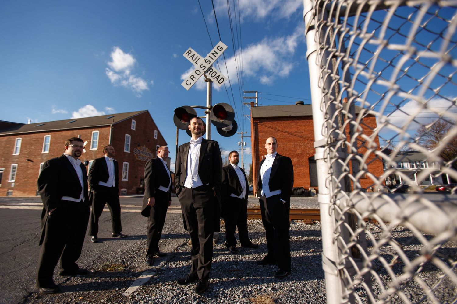 Groomsmen gather at railroad crossing in stylish suits.