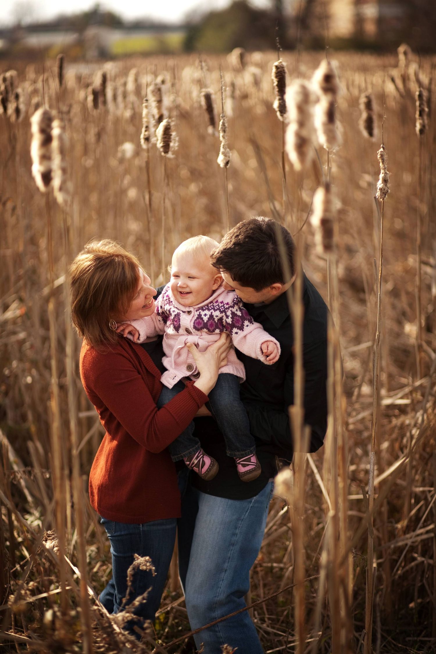 A candid moment of affection amongst tall cattails in a field at golden hour.