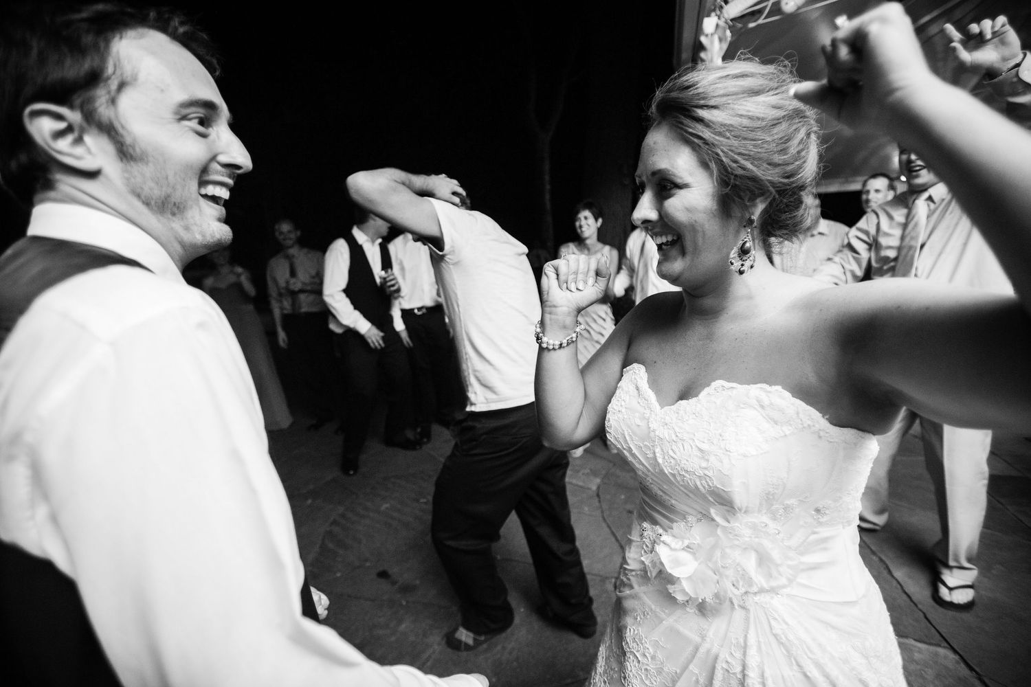 A joyful candid black and white photo of wedding guests dancing enthusiastically at a reception.