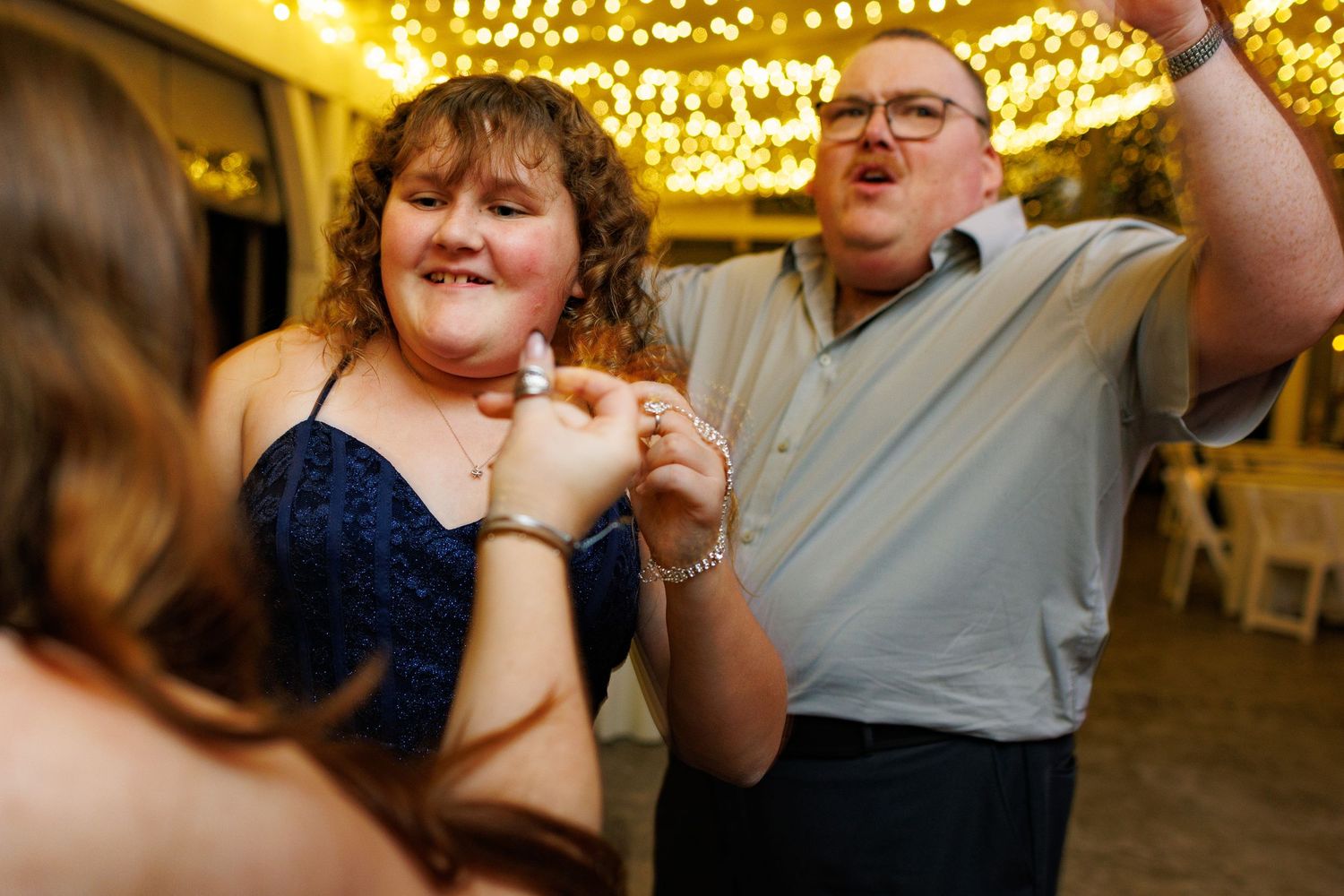 Joyful dancing and celebration at a wedding reception under warm string lights.