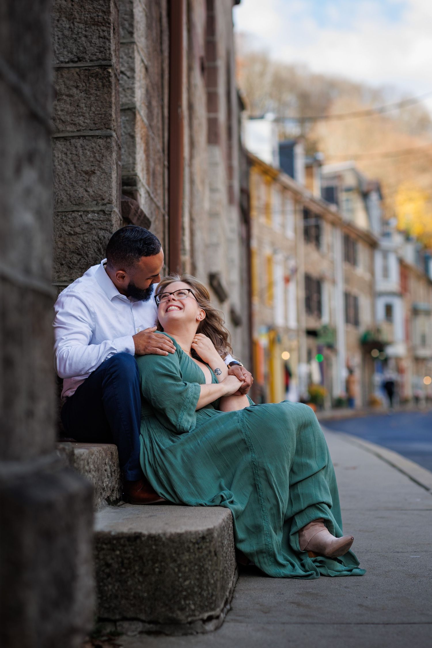 A romantic couple shares an intimate moment while sitting on stone steps in a historic street setting.